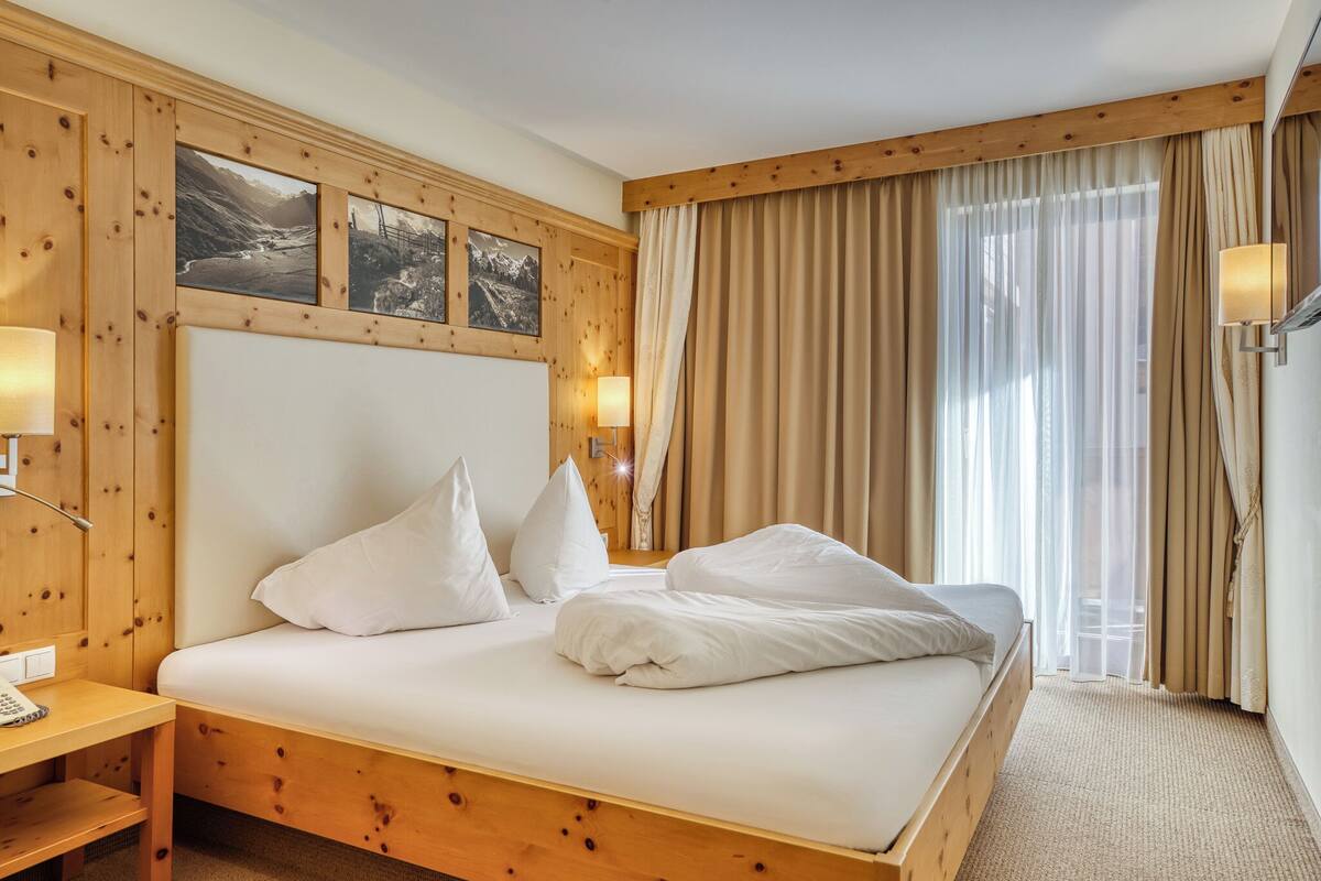 A neatly made bed with white linens and pillows, wooden headboard, and a wooden nightstand with a lamp.