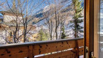 Un balcon en bois offrant une vue sur des montagnes enneigées et un bâtiment traditionnel doté d’un clocher.