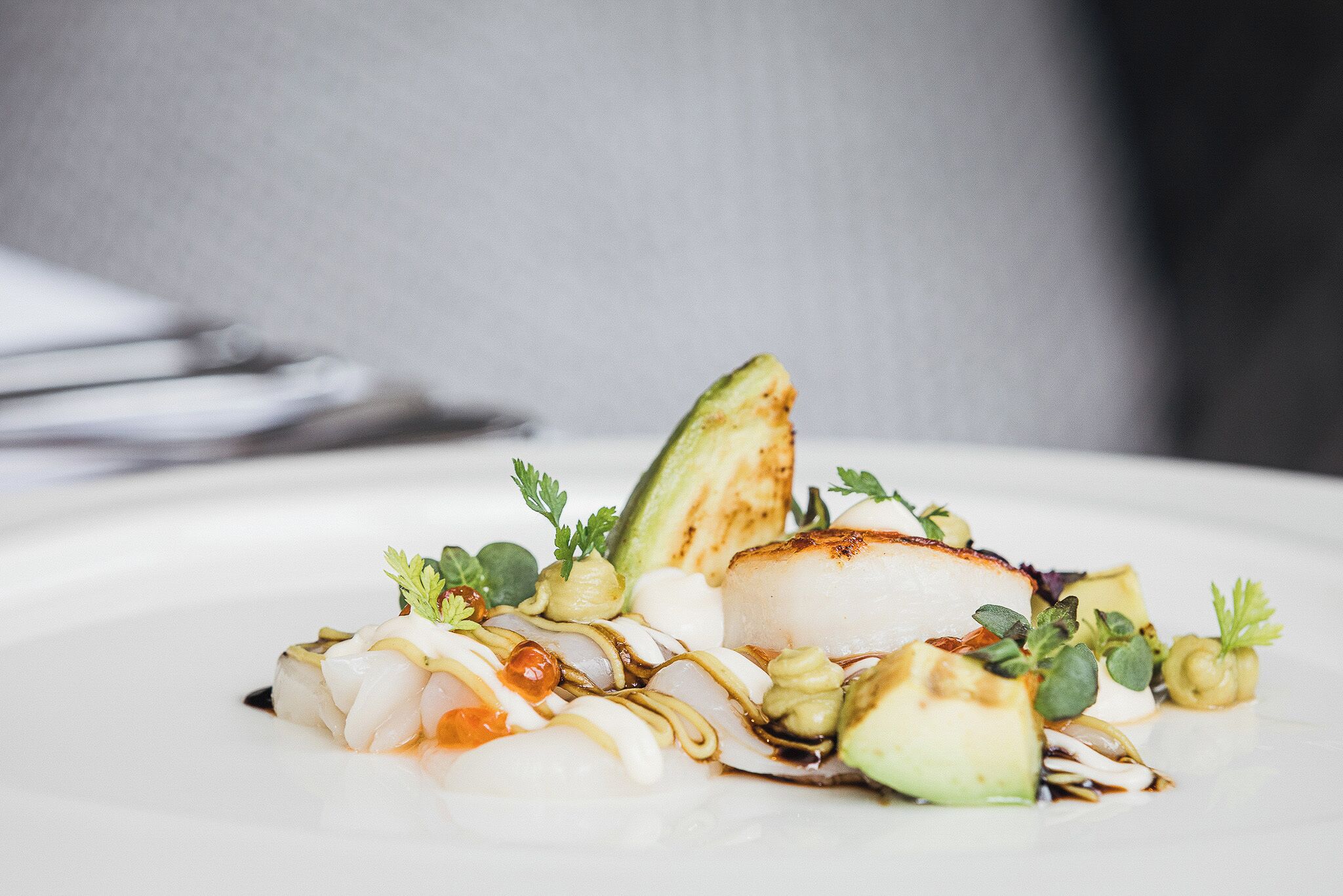 Un plato blanco con un plato de mariscos, que incluye pescado a la plancha y verduras, adornado con hierbas.