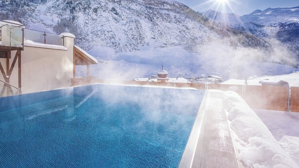 A snow-covered mountain landscape with a clear sky and a pool area featuring a hot tub. - Hotel Klausnerhof (Tux)