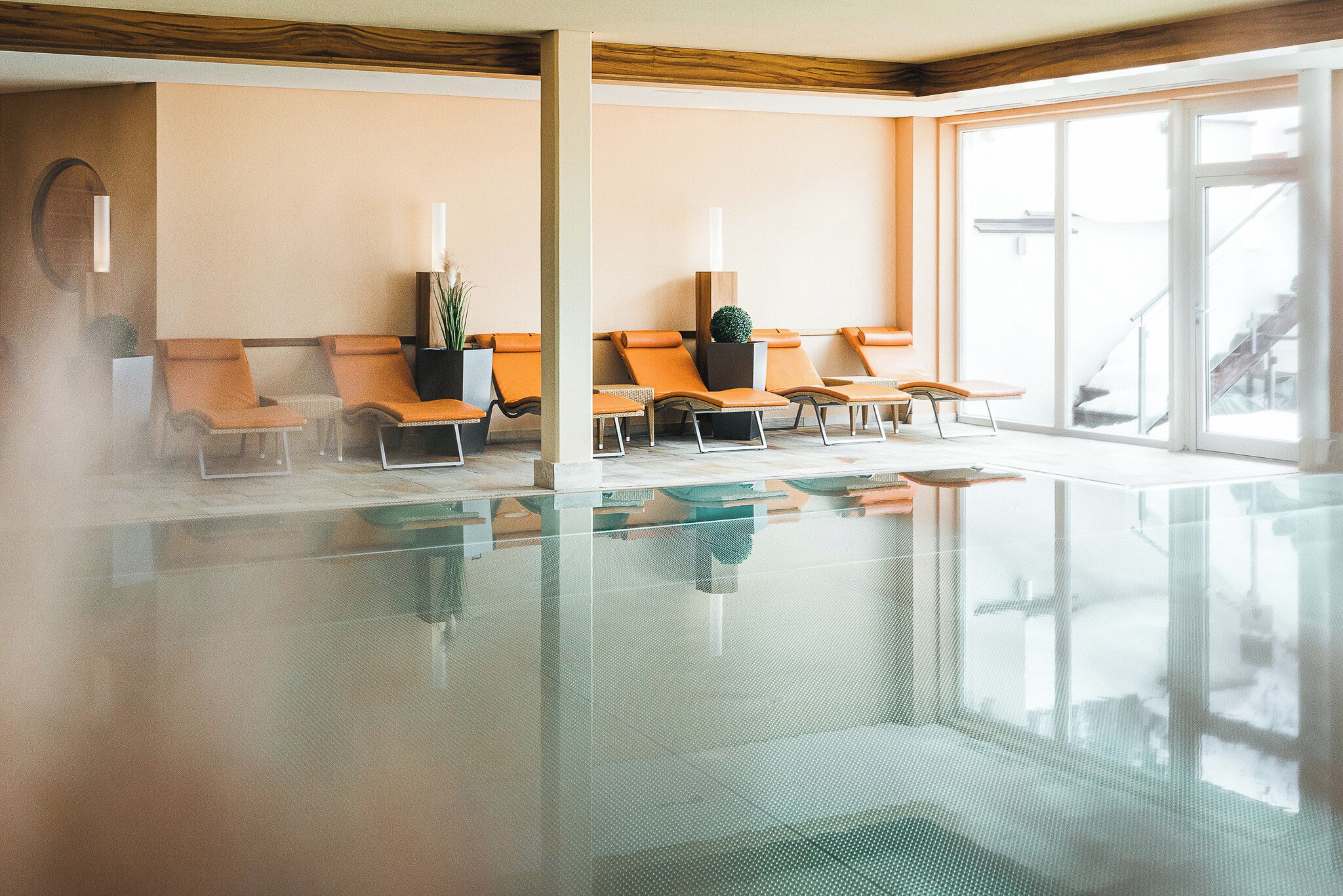 Zona de spa con piscina envuelta en cristal, sillones de descanso naranja y un ventanal con vistas al exterior.