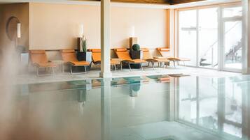 Zona de spa con piscina envuelta en cristal, sillones de descanso naranja y un ventanal con vistas al exterior.