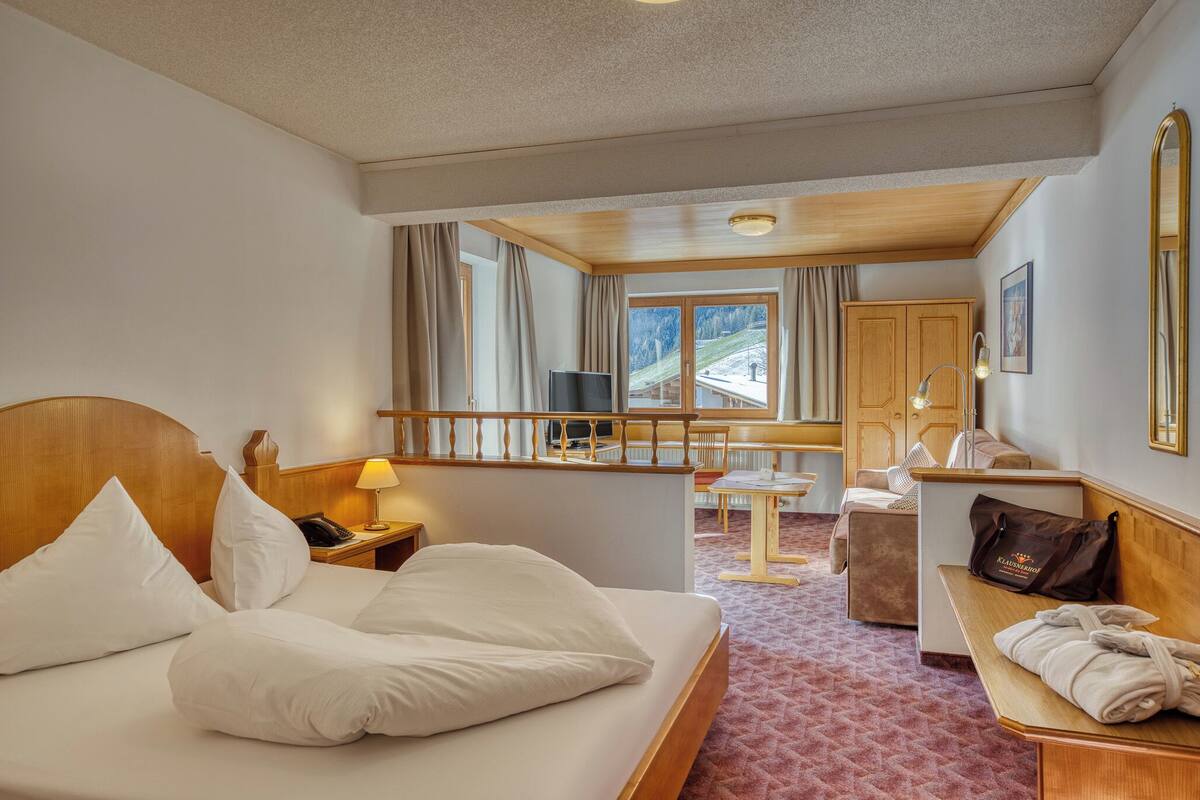 A hotel room with a bed, a desk, a chair, a small table, and a view of a snowy landscape through the window.