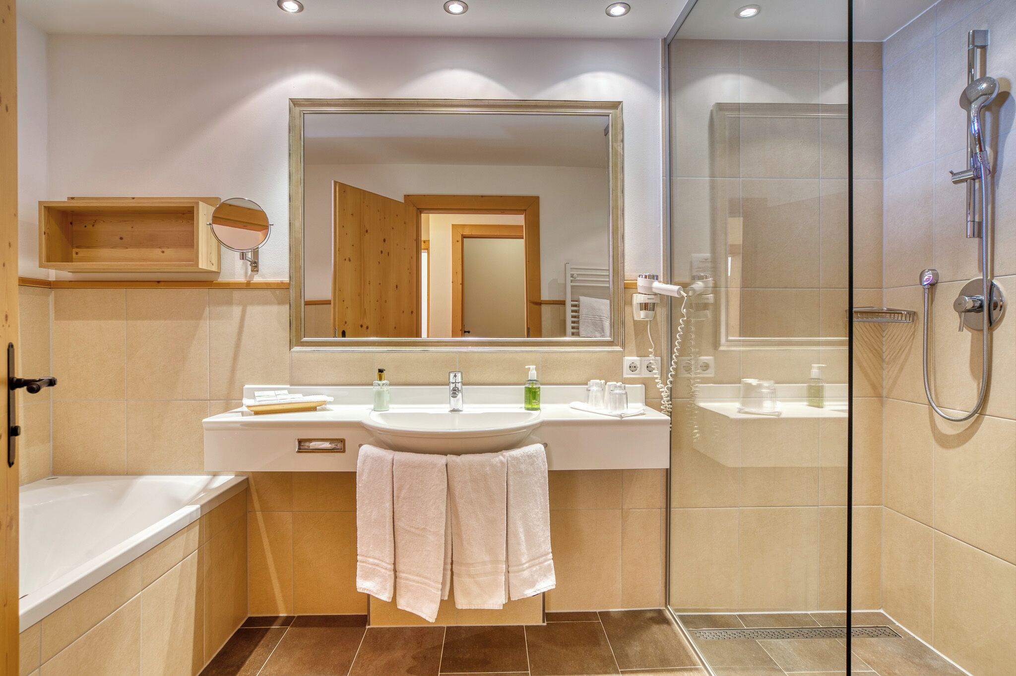 A modern bathroom with a large mirror, a sink with toiletries, a shower, and a bathtub.