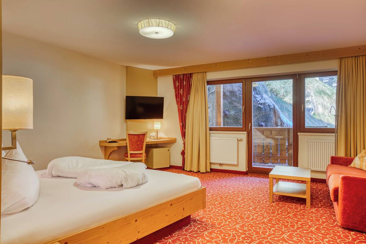 A hotel room with a bed, desk, chair, TV, and a view of a waterfall through large windows.