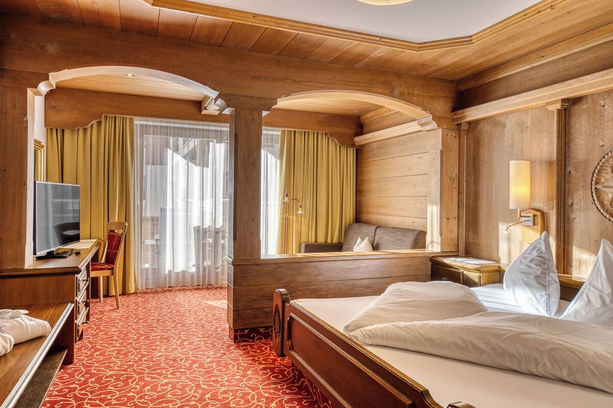 A hotel room with a wooden interior, a bed, a desk with a chair, a television, and a window with curtains.