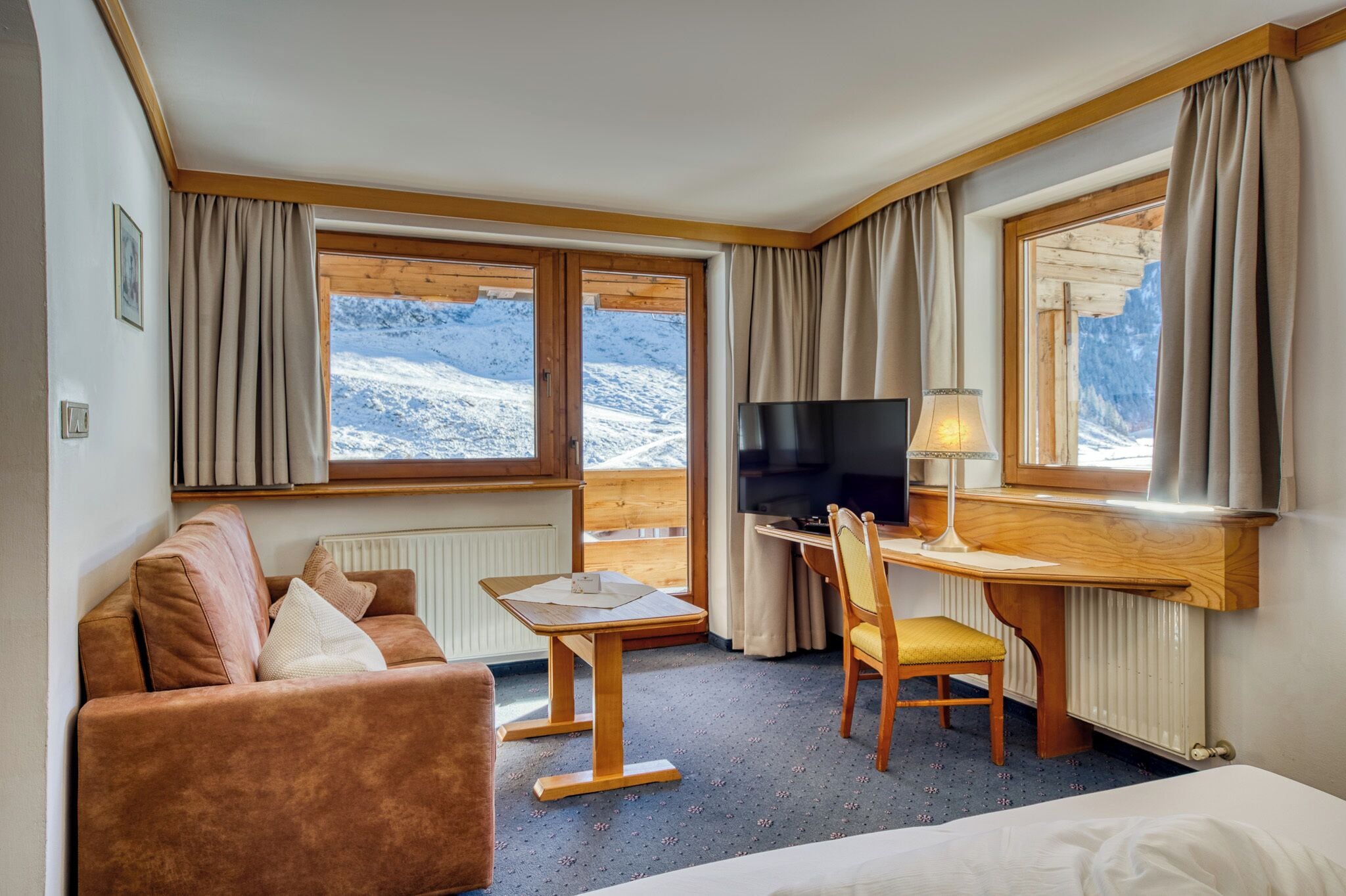Une chambre d’hôtel équipée d’un canapé, d’un bureau avec une chaise, d’une télévision et de grandes fenêtres avec des rideaux.