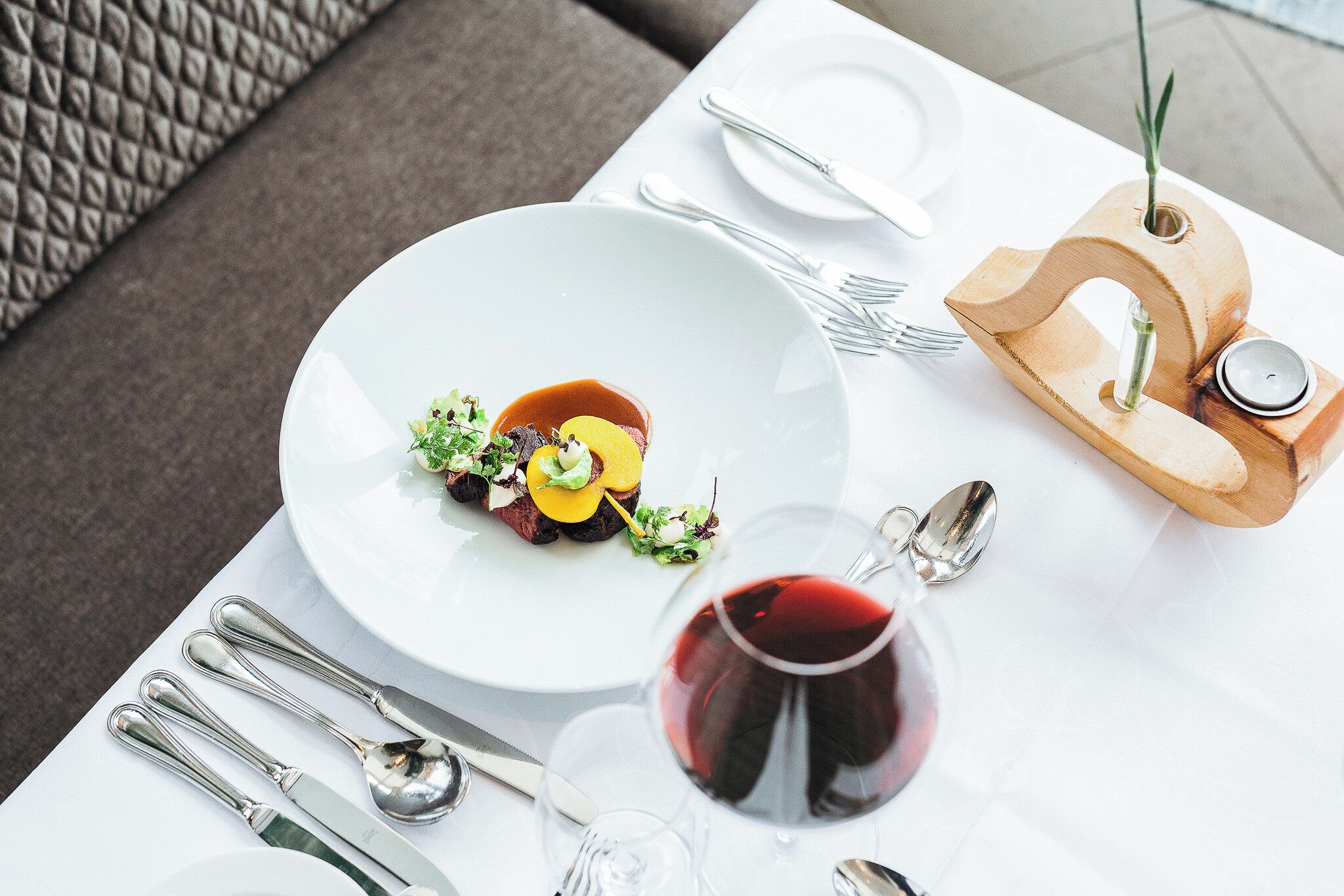 A dining table with a white plate of food, a glass of red wine, and silverware.