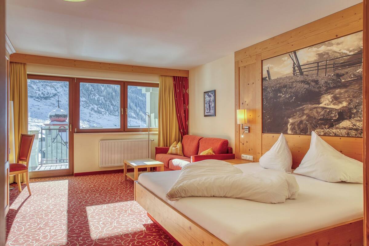 A hotel room with a large bed, a sofa, a small table, and a view of a snowy mountain.