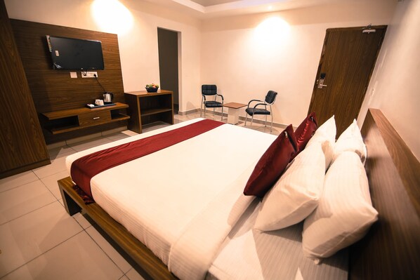 A modern hotel room with a large bed, a TV mounted on the wall, a desk with a chair, and a wooden wardrobe.