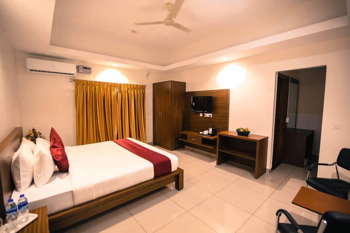 A hotel room with a bed, a desk, a chair, a TV, a wardrobe, and an air conditioning unit.
