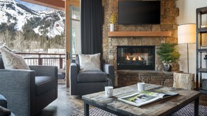 A cozy living room with a stone fireplace, comfortable seating, and a view of a snowy mountain. - Outpost: Crystal Springs 306 - Ski-In/Ski-Out! (Teton Village)