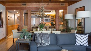A modern living room with a grey sofa, a wooden coffee table, and a dining area with a chandelier. - Outpost: Crystal Springs 306 - Ski-In/Ski-Out! (Teton Village)