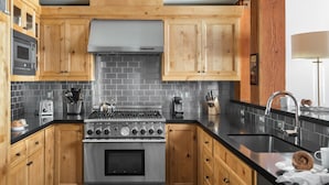 A kitchen with wooden cabinets, a stainless steel stove, and a black countertop. - Outpost: Crystal Springs 306 - Ski-In/Ski-Out! (Teton Village)