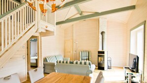 Amplia sala de estar con una mesa de comedor de madera, sofás a rayas, chimenea y una escalera que sube a un nivel superior.