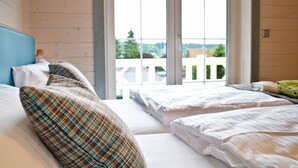 Una habitación con dos camas, ventanas amplias y vistas a una cerca blanca y follaje exterior.