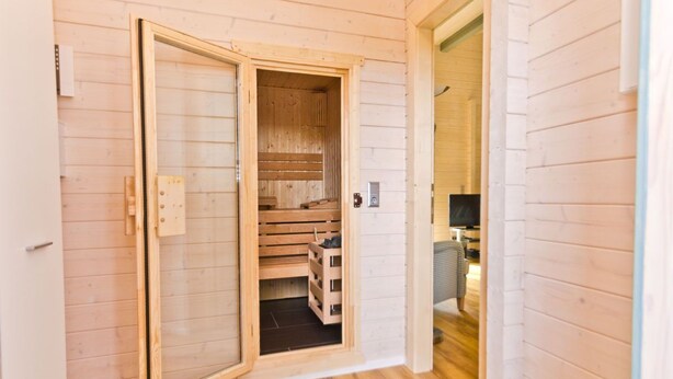 Interior de madera con una sala de sauna, suelo de madera y una puerta visible que da a otra habitación.
