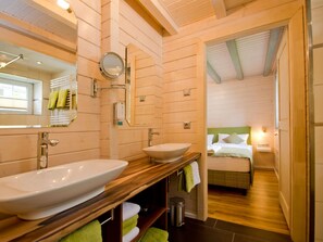A wooden cabin-style room with two large sinks, a bed with green bedding, and a small bedside table.