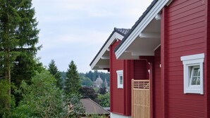 Una casa roja con un portón de madera, rodeada de follaje y árboles.