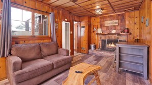 A cozy cabin interior with a wooden interior, a fireplace, a sofa, and a coffee table. - Shore Acres Lodge #451 (Big Bear Lake)