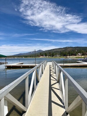A wooden pier leading to a dock with calm water, surrounded by a forested hillside and clear blue sky. - Shore Acres Lodge #451 (Big Bear Lake)