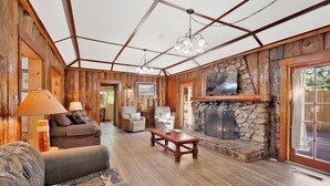 A rustic interior with a stone fireplace, wooden walls, and a cozy seating area with a sofa and armchairs. - Shore Acres Lodge #451 (Big Bear Lake)