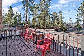 A wooden deck with red Adirondack chairs, overlooking a forested area with cabins and a playground. - Shore Acres Lodge #451 (Big Bear Lake)