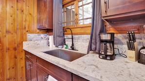 A kitchen with wooden cabinets, a marble countertop, a sink, a coffee maker, and a knife block. - Shore Acres Lodge #451 (Big Bear Lake)