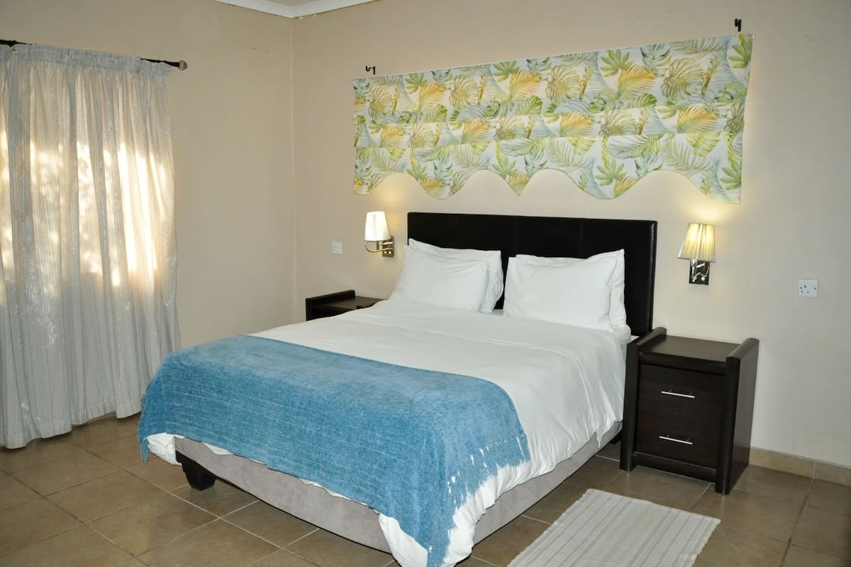 A bedroom with a bed, two bedside tables with lamps, a curtain, and a wall tapestry.
