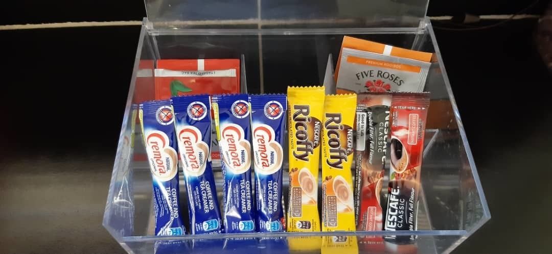 A clear plastic container with various coffee creamer packets and a few other items.