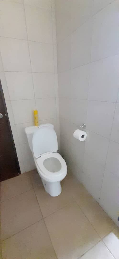 A small, tiled bathroom with a white toilet, a toilet paper holder, and a visible door frame.