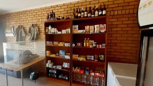 A room with a brick wall, wooden shelves stocked with various items, and a table with a pot.