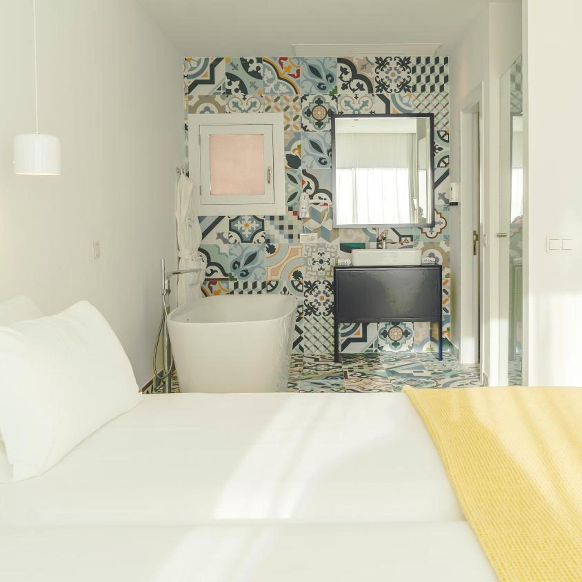 A bedroom with a bed, a white sink, a mirror, and a patterned wall.