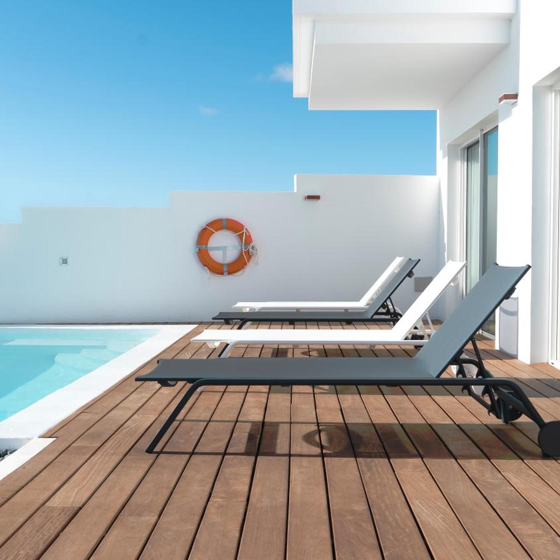 Una terraza de madera con sillones de descanso y una piscina.