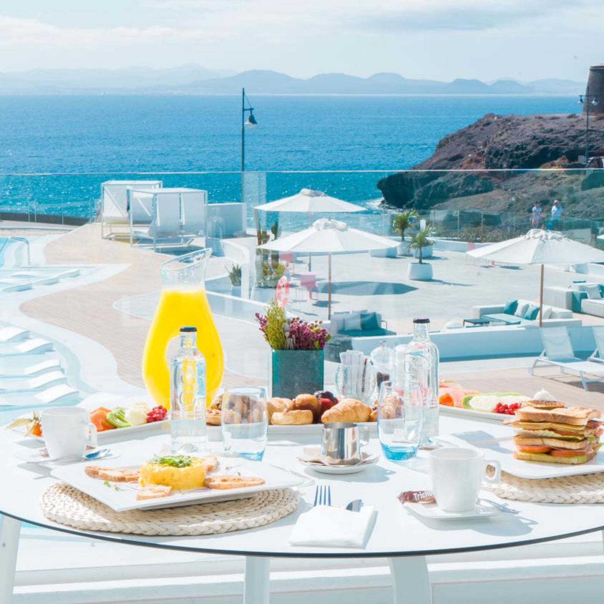 A table set with breakfast items, a glass of orange juice, and a view of the ocean.