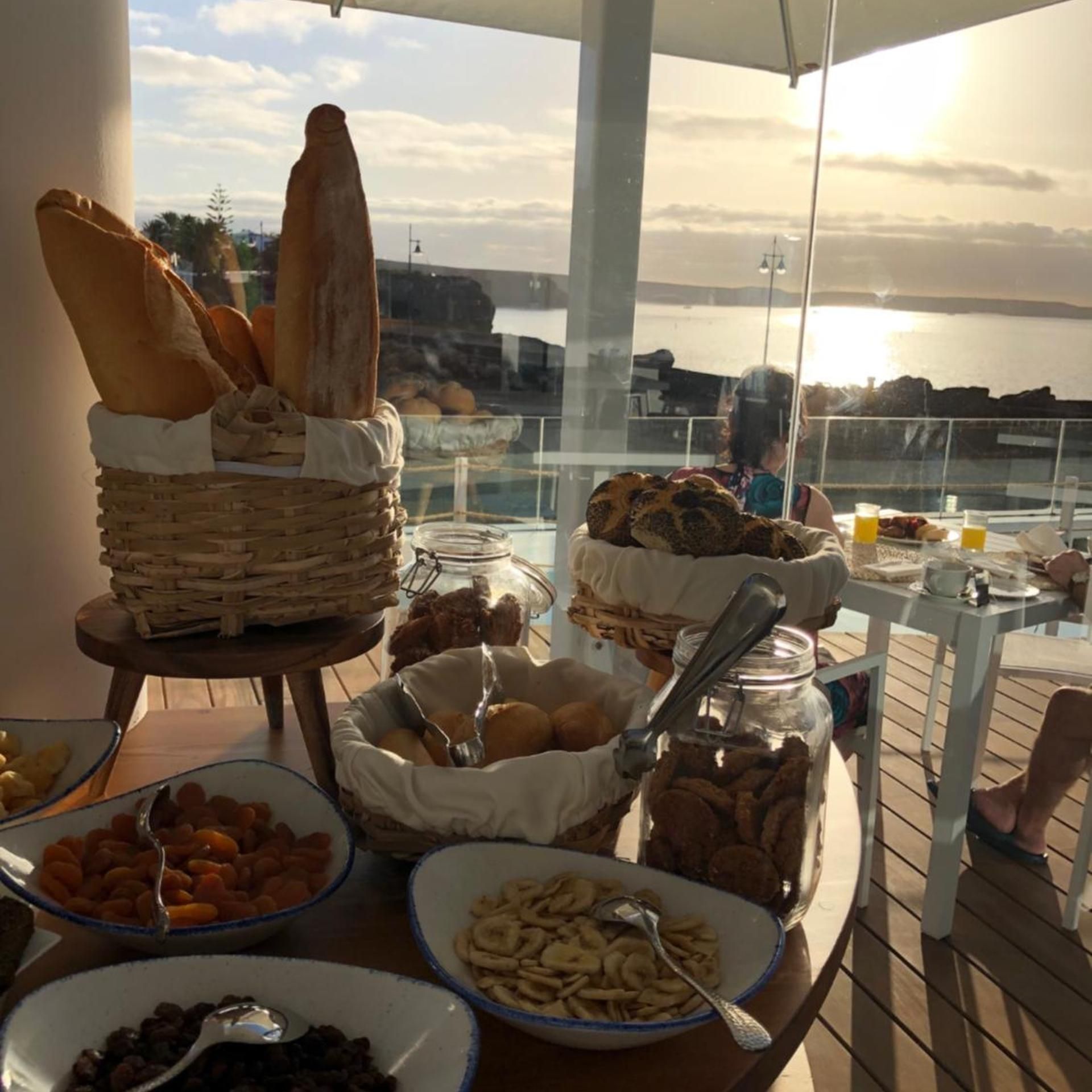 A buffet table with various food items and a view of the sea.