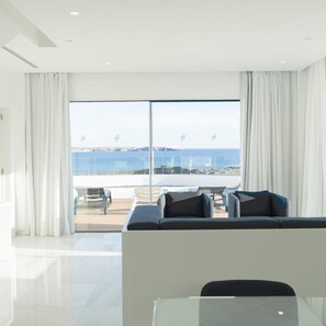 Un salon moderne doté d’une grande porte-fenêtre coulissante donnant sur un balcon avec vue sur la mer.