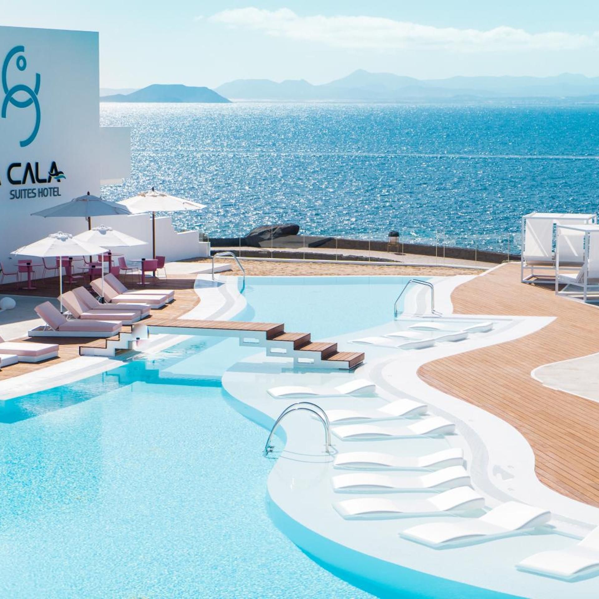 A pool area with lounge chairs and umbrellas, a sign for 'CALA SUITES HOTEL', and a view of the sea.