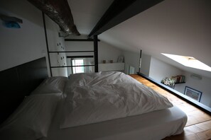 Une chambre à coucher avec un lit, un plancher en bois, un puits de lumière et un mur blanc.