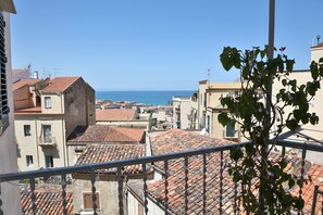 A view of terracotta-tiled rooftops and buildings with a clear blue sky and sea in the background.