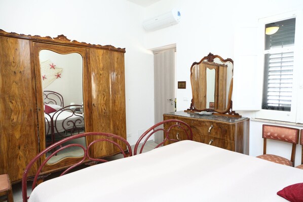A bedroom with a wooden wardrobe, a bed, a dresser, and a mirror.