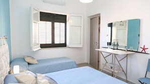 Une chambre avec deux lits simples, un bureau avec un miroir et une fenêtre avec des stores.