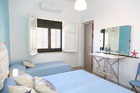 A bedroom with two single beds, a desk with a mirror, and a window with blinds.