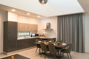 A modern kitchen with dark cabinets, a microwave, and a stove. There is a dining table with chairs and a window overlooking the kitchen. - Napa Hills Seaview Villas (Ayia Napa)