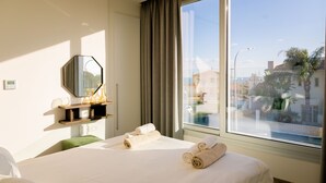 Ein Hotelzimmer mit einem großen Bett, einem Spiegel, einem Fenster mit Vorhängen und Blick nach draußen.