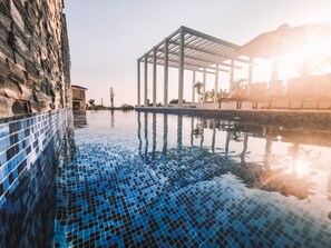 A swimming pool with clear blue tiles, a stone wall on one side, and a pergola structure in the background. - Napa Hills Seaview Villas (Ayia Napa)