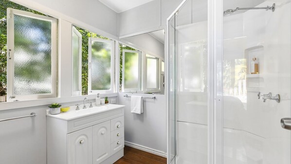 Un baño con tocador blanco, cabina de ducha de vidrio y ventanas con vidrio esmerilado.