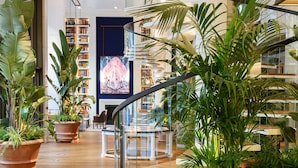 Un espacio interior moderno con suelo de madera, plantas en macetas, una escalera y una estantería al fondo.