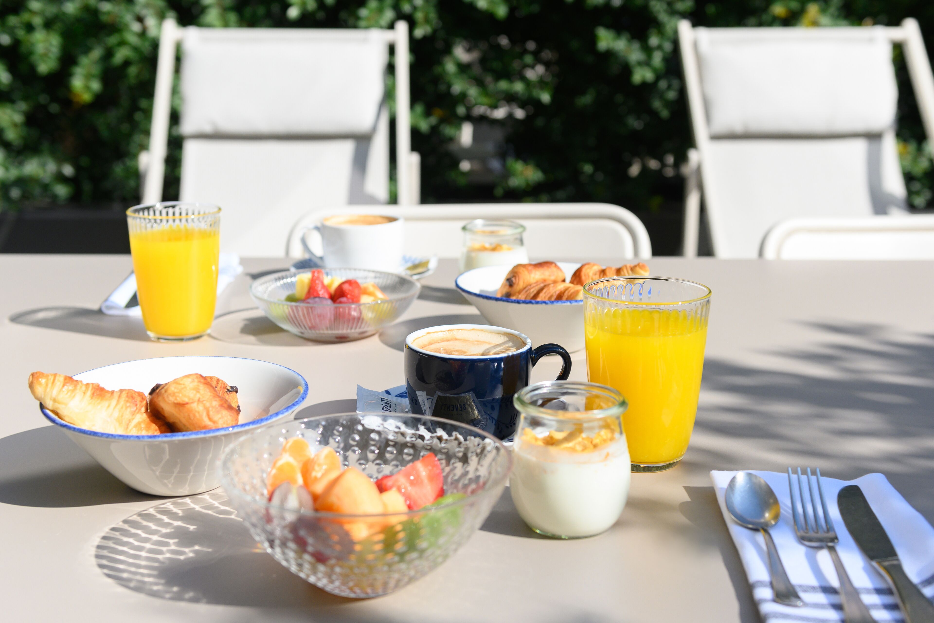 Una mesa de desayuno con cruasanes, fruta, café y jugo de naranja.