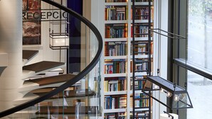 Un interior moderno con una escalera en espiral, un sofá rojo, un sillón blanco y una estantería llena de libros.